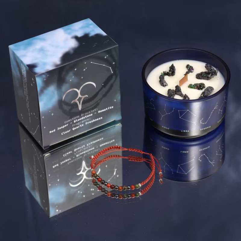 Vela energética del zodiaco Aries con pulsera de piedras preciosas y vaso de vidrio azul con constelaciones.