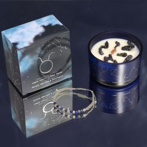 Vela energética del zodiaco Tauro con pulsera de piedras preciosas y vaso de vidrio azul con constelaciones.