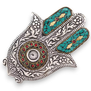 Portainciensos Hamsa en metal con detalles rojo y verde para varillas sobre superficie decorativa.
