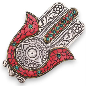 Portainciensos Hamsa en metal con detalles rojo y verde para varillas sobre superficie decorativa.