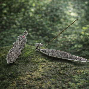 Portainciensos tibetano alargado de metal con grabado decorativo para varillas de incienso sobre superficie plana.