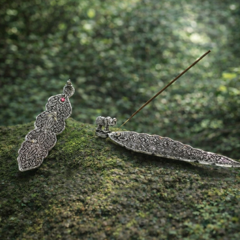 Portainciensos tibetano alargado de metal con grabado decorativo para varillas de incienso sobre superficie plana.