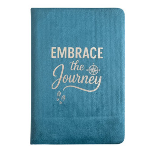 Vista frontal del cuaderno de terciopelo azul claro con el mensaje Embrace the Journey y símbolos de brújula y huellas.